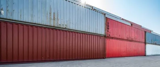 Dependable Inventory: Rugged Containers for Government Field Use Close-up of stacked shipping containers in red, maroon, and gray, illustrating various used conditions for secure field storage.
