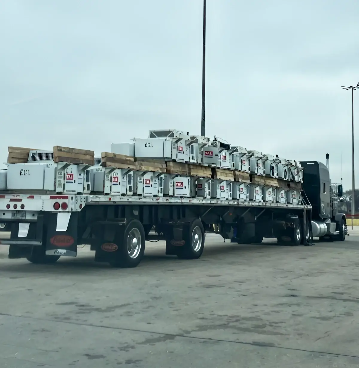 A large truck loaded with multiple undermount chassis gensets on a flatbed trailer, secured with wooden braces for transport.