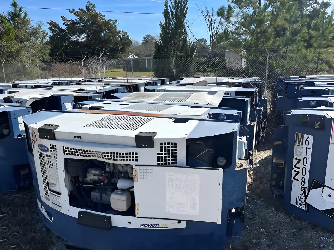 Several used Carrier refrigeration units with partially open covers, stored in an outdoor yard, ready for use in refrigerated transport.