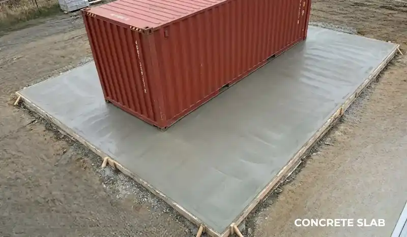 Red shipping container centered on a solid, freshly poured concrete slab foundation.