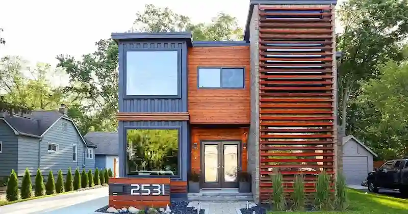 Luxurious, multi-story container home with wood cladding, large windows, and a slatted exterior in a suburban neighborhood.