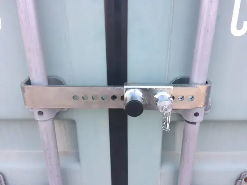 Silver adjustable crossbar lock clamped across the vertical locking rods of a container.