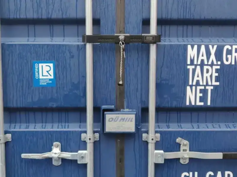Close-up of a blue shipping container door with a secure lock box protecting a padlock.