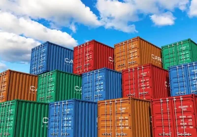 Colorido render 3D de contenedores de transporte (rojo, azul, naranja, verde) apilados en lo alto contra un cielo azul brillante.