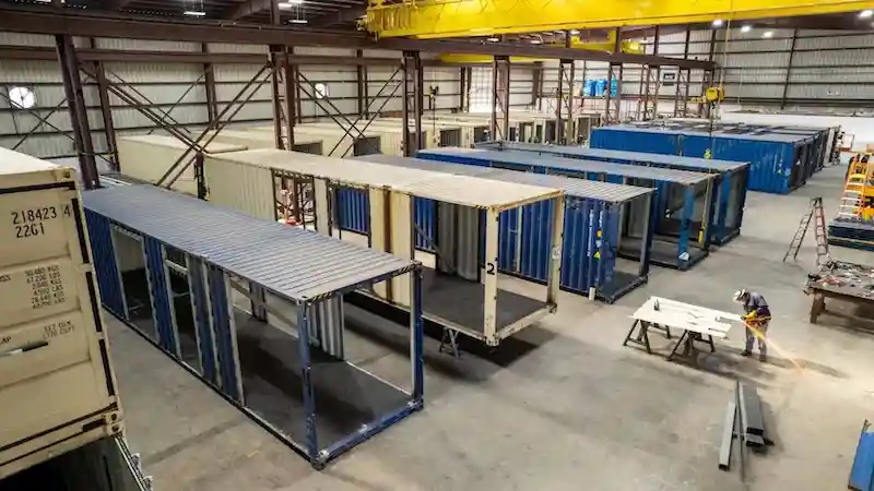 Overhead view of a shipping container manufacturing workshop with workers and cranes.