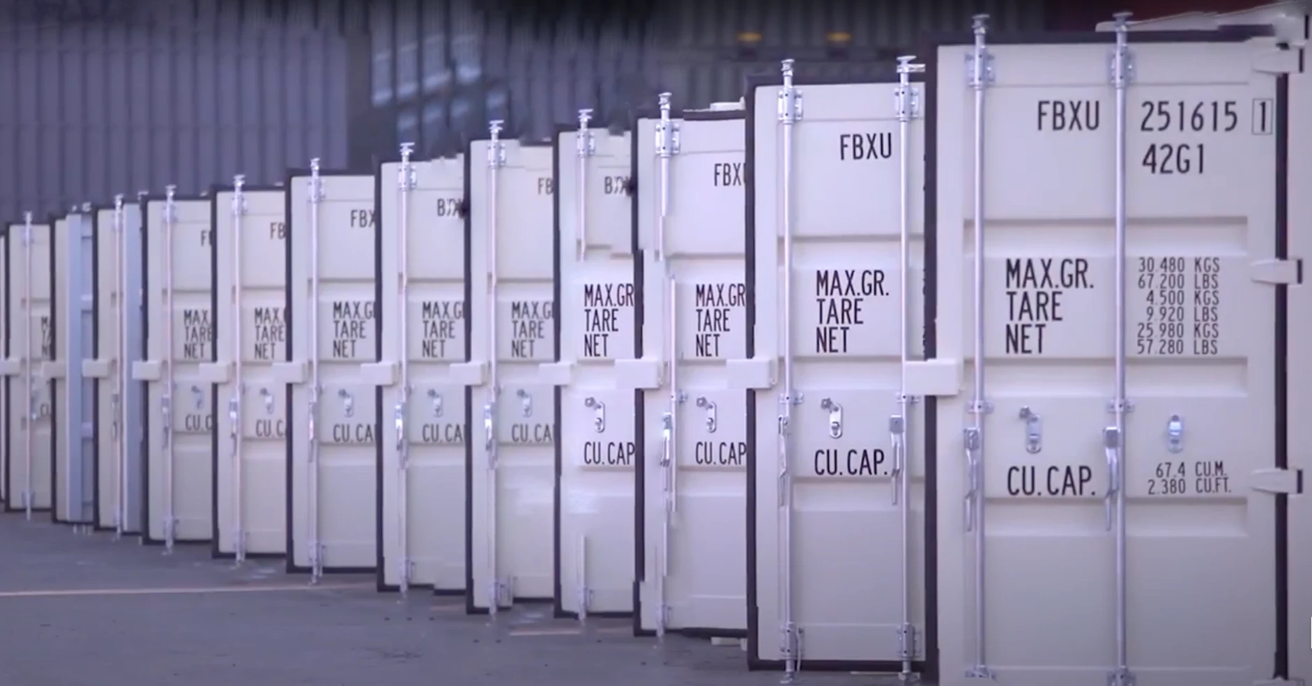 A row of beige shipping containers with weight and capacity specifications clearly displayed, arranged at an outdoor storage facility