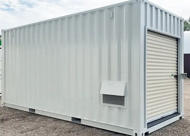 Clean white shipping container with an installed roll-up door and a square louvered vent for passive air circulation.