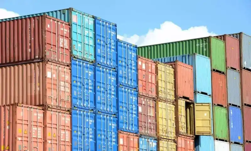 Coloridas pilas de contenedores de transporte rojos, azules, verdes y amarillos bajo un cielo brillante, que simbolizan un enorme volumen de inventario.