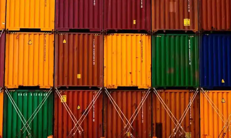 Primer plano de contenedores de transporte multicolores firmemente apilados y asegurados con barras de cierre, que simbolizan un inventario global controlado.