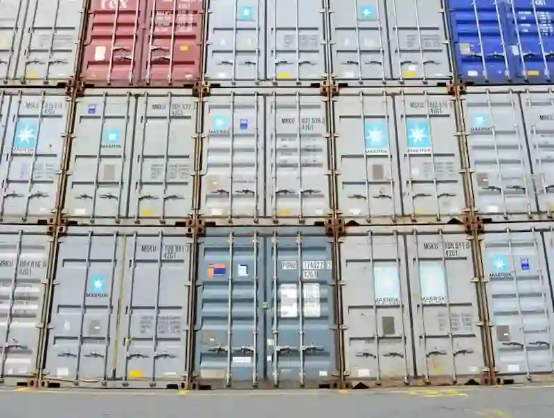 Close-up of stacked containers showing rust, ownership logos, corner castings, and identification codes, detailing wear and tear.