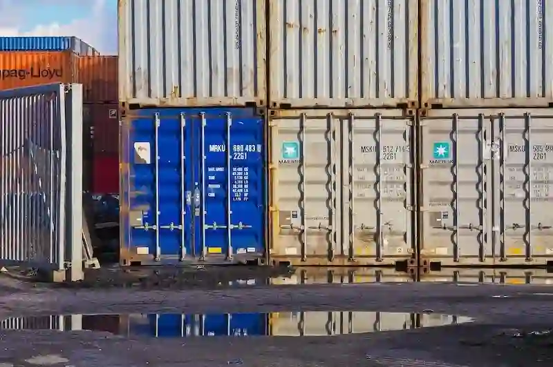 Close-up of blue and gray stacked containers showing identification codes, door mechanisms, and signs of rust and wear. 