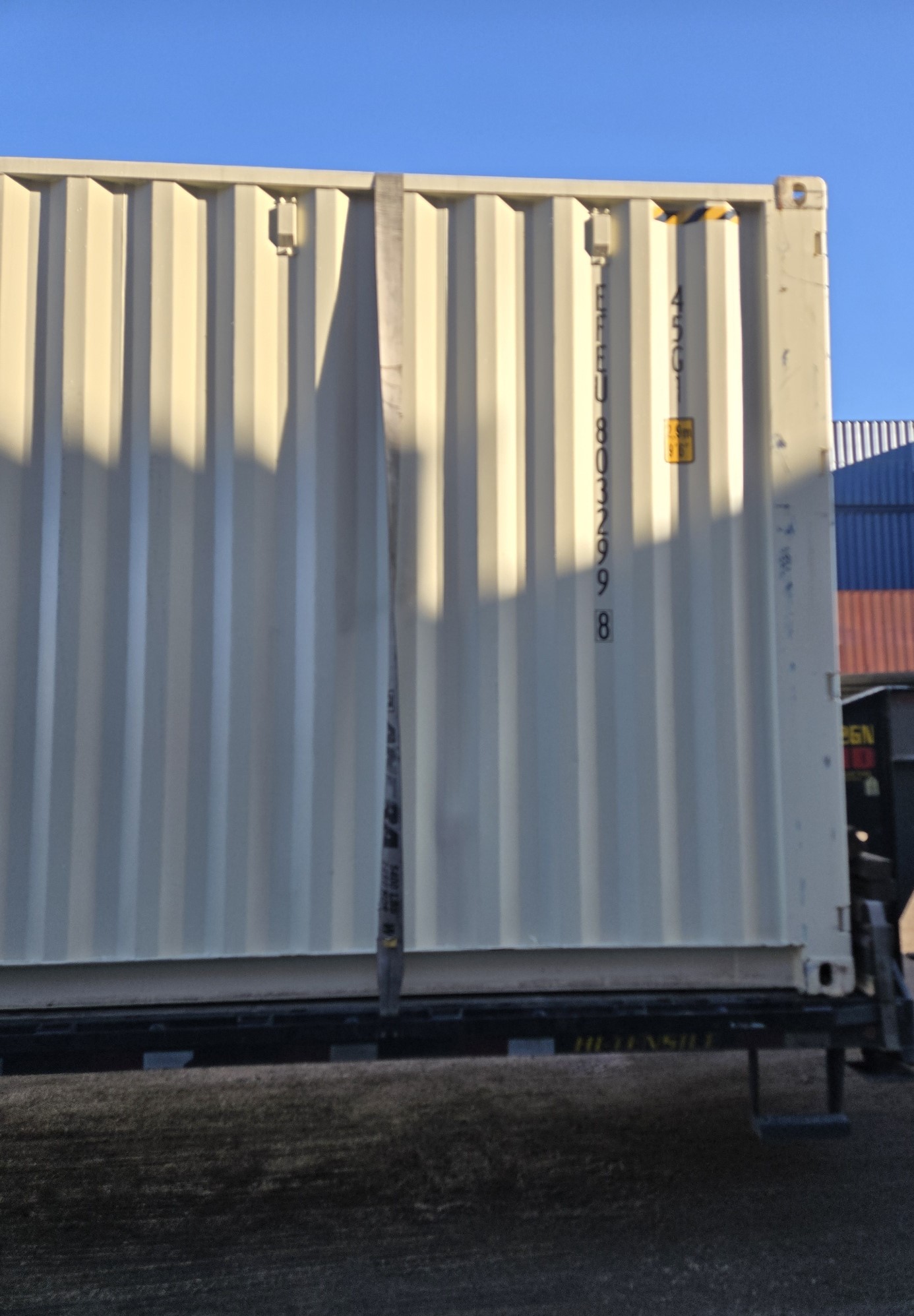 Close-up side view of a white 40ft high cube new shipping container on a tilt-bed trailer in a yard setting