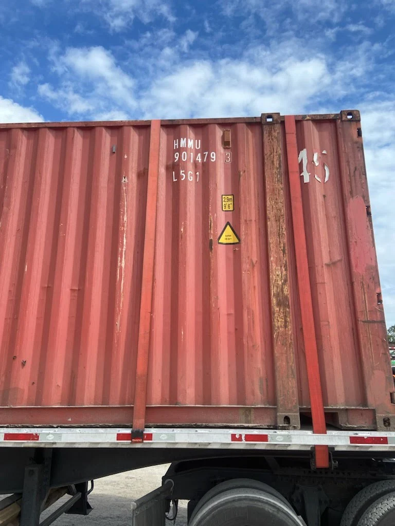 Side view of a 45ft high cube used shipping container strapped on a flatbed trailer in a container yard