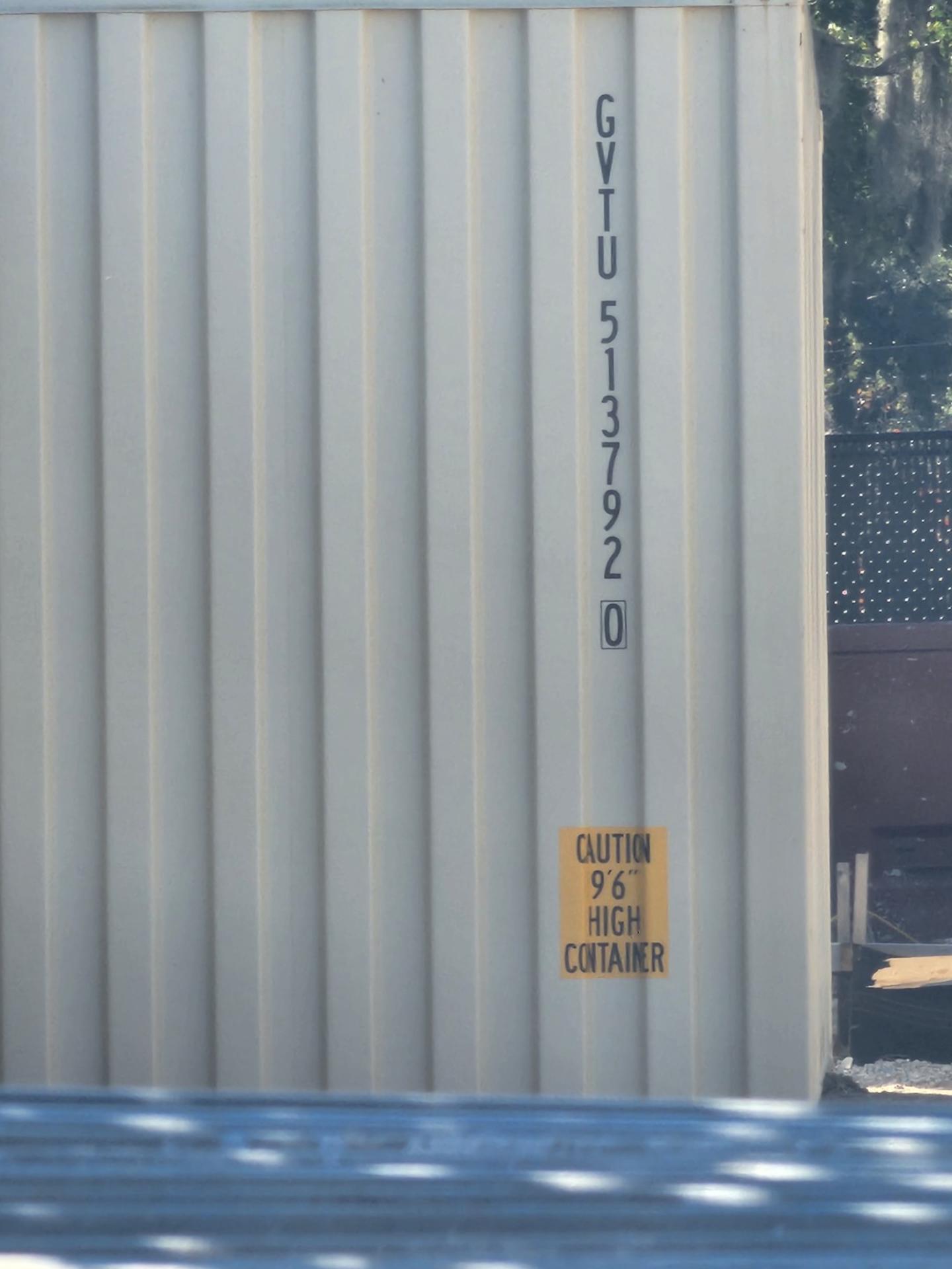 Side wall of a beige 40ft high cube container positioned at ground level near a fenced site